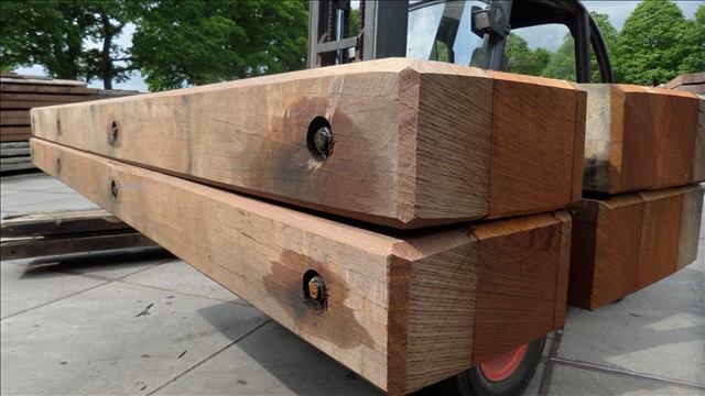 Forklift transporting hardwood ekki timber mats in an outdoor industrial storage yard.