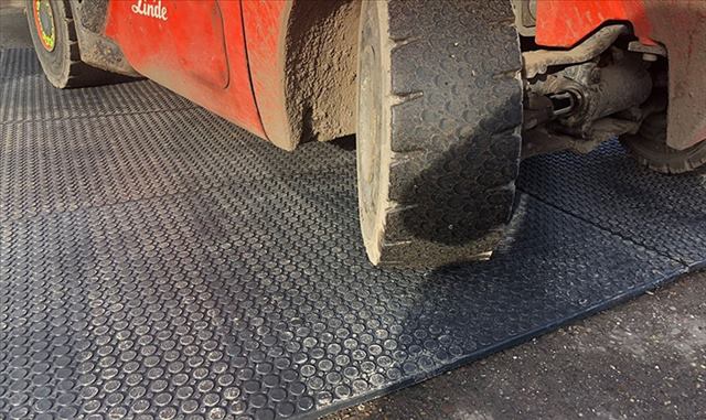 Heavy-duty forklift driving over interlocking rubber mats, demonstrating their durability in an industrial yard.