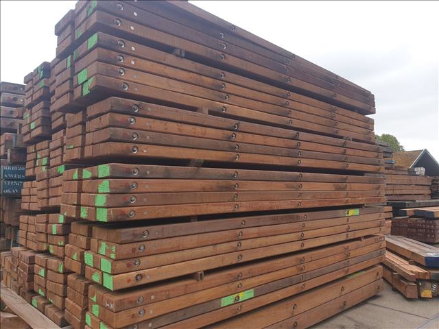 Timber mats stacked outdoors with green-painted ends for identification, stored in a large yard.