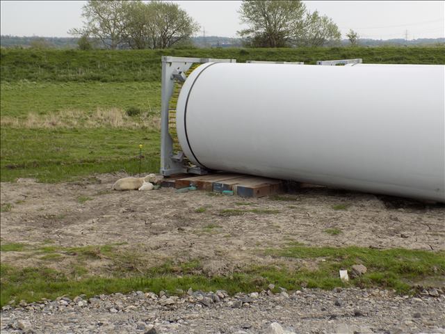 Wind turbine base securely resting on timber mats in a grassy field, ensuring stability. While a sheep and lamb sleep against them.