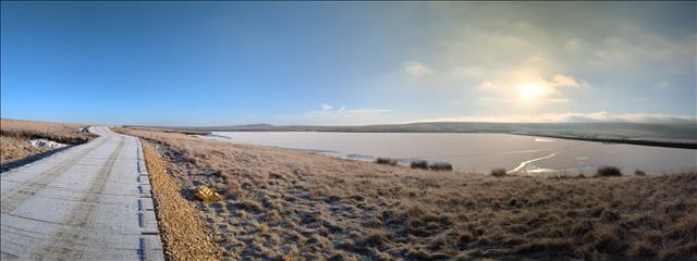 Frost-covered timber mat road winding through a wintry landscape with a frozen lake in the distance.