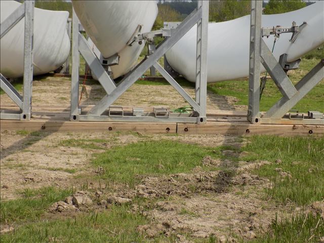 Close-up of wind turbine components stabilised by timber mats and metal frames in a field.